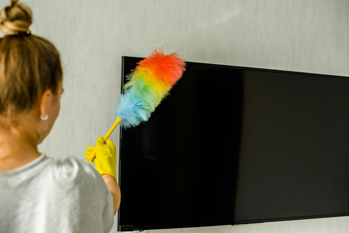 Mujer limpiando televisión con plumero colorido ilustrando tendencias hogareñas superadas por millennials.