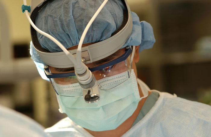 Médico con equipo quirúrgico y mascarilla realizando procedimiento en hospital, representando errores hospitalarios graves.