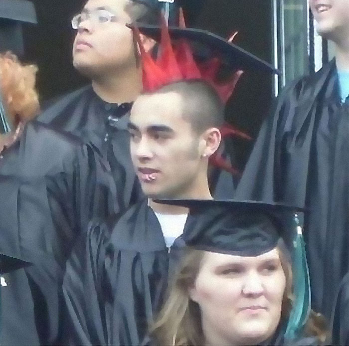 Joven con peinado punk y pendiente en ceremonia de graduación, imagen realmente incómoda pero divertida.