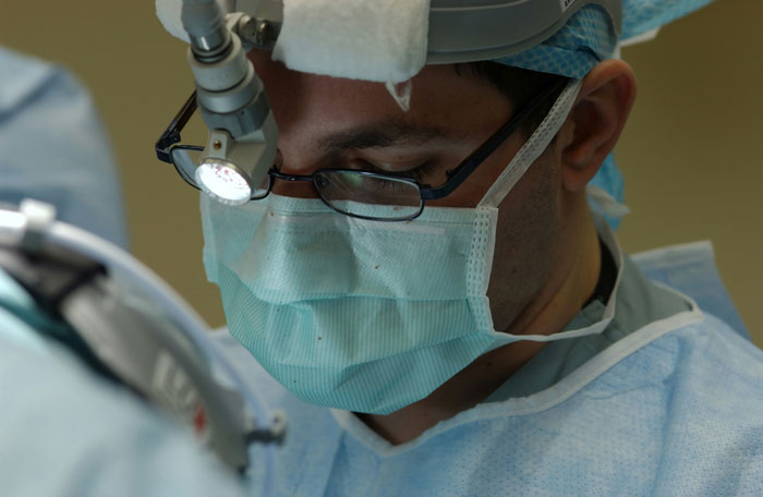Médico cirujano con mascarilla y gafas realizando procedimiento en hospital durante intervención quirúrgica importante.