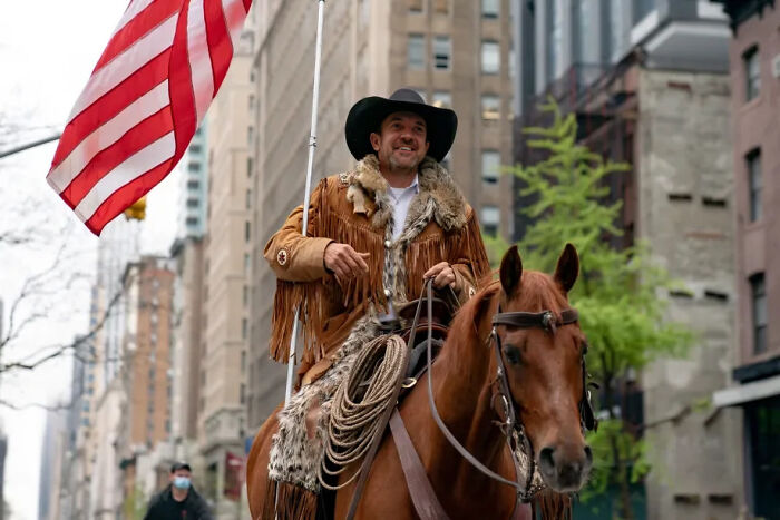Hombre vestido de vaquero montando un caballo en la ciudad, imagen relacionada con personas estúpidas en el trabajo siendo despedidas.