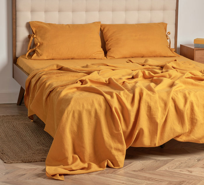 Cama con ropa de cama amarilla arrugada en habitación moderna mostrando tendencias hogareñas de la vieja escuela.