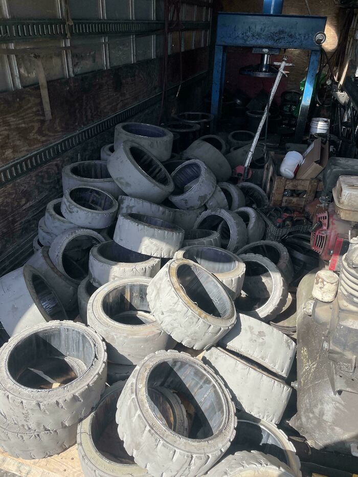 Neumáticos usados apilados en un taller desordenado, mostrando un día difícil en el trabajo con equipos industriales viejos.
