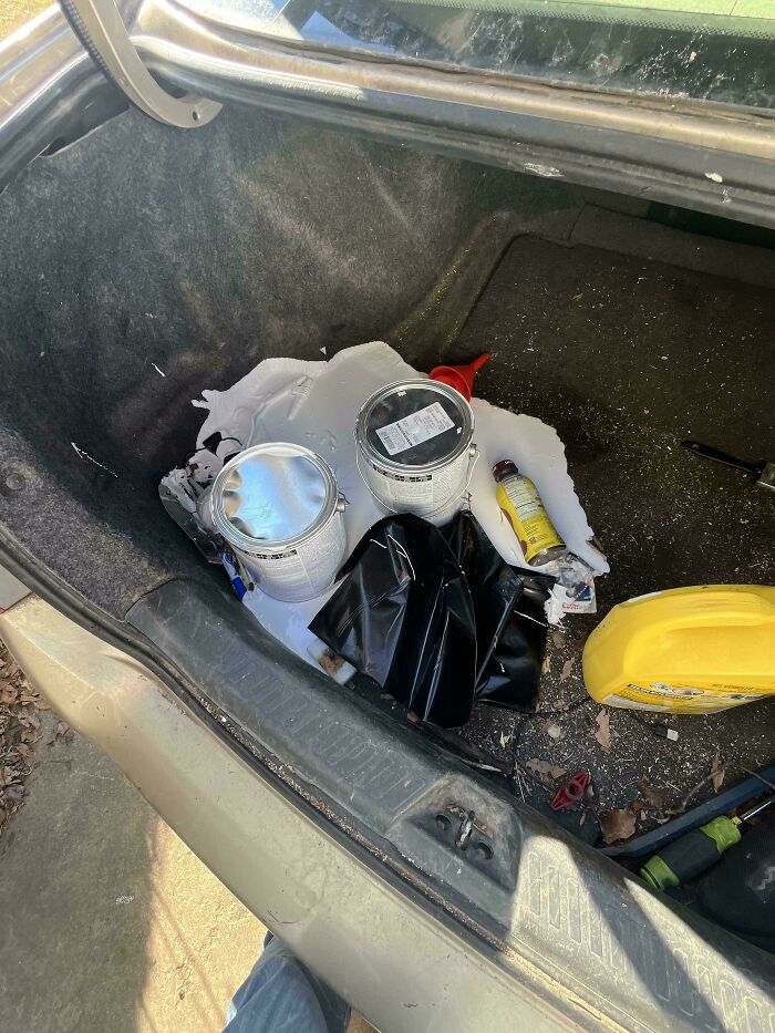 Bote de pintura derramado en el maletero del coche, mostrando un día peor en el trabajo con desastre y suciedad.