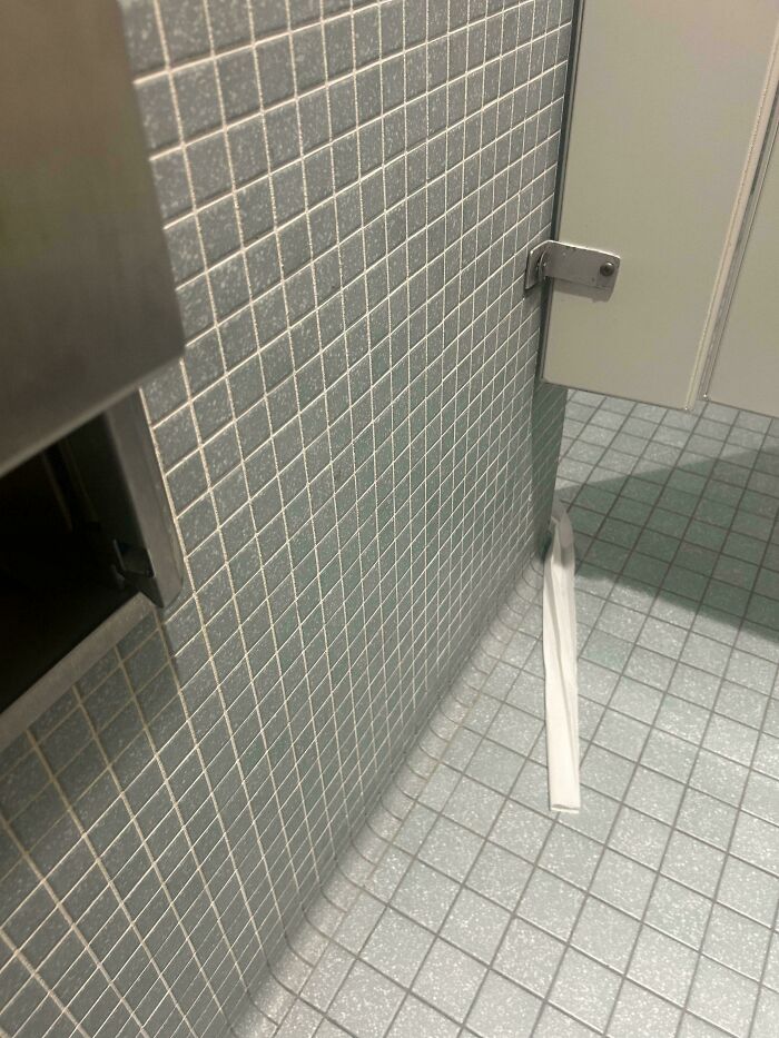 Papel higiénico atrapado bajo la puerta del baño en una oficina, ejemplo de día peor en el trabajo para personas.