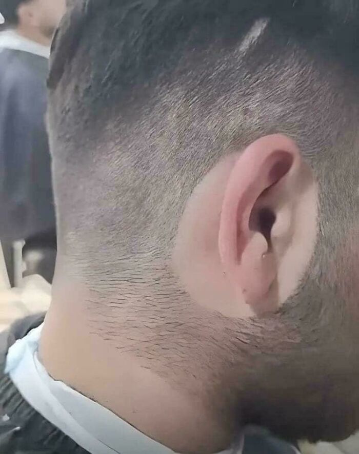 Hombre con corte de cabello irregular y mal acabado en salón de belleza causando arrepentimiento y disgusto.