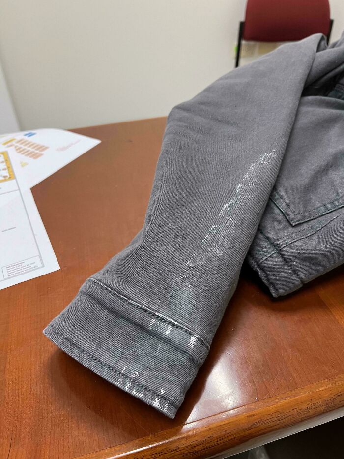 Mancha blanca en manga de chaqueta gris sobre mesa de madera, representando un día peor en el trabajo.