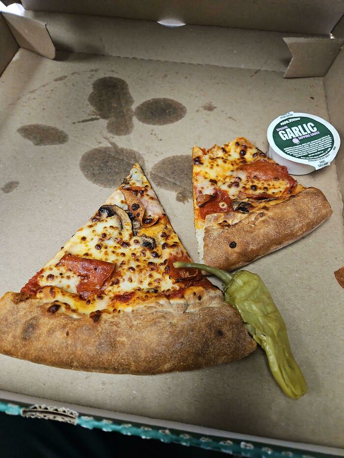 Dos rebanadas de pizza en caja con salsa de ajo y chile, ejemplo de personas que llevan un día peor en el trabajo que tú.