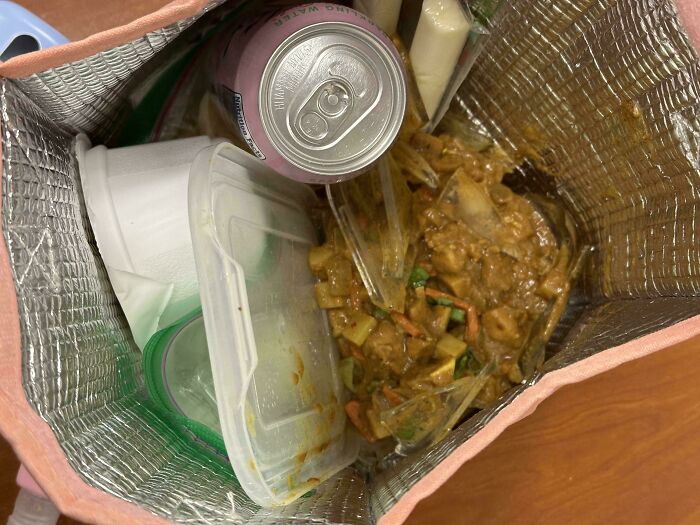 Contenedor térmico con comida derramada y latas, mostrando un mal día en el trabajo con problemas para la comida.