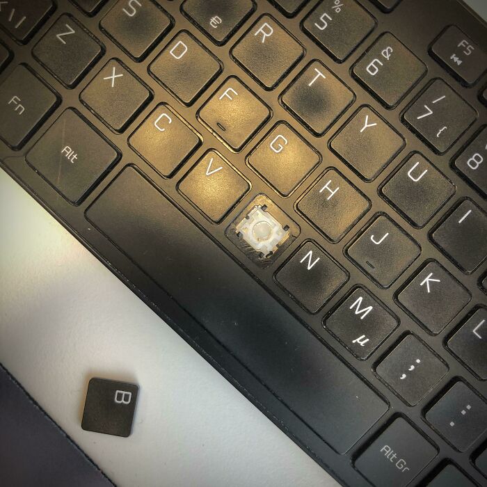 Teclado con tecla B faltante y desprendida, mostrando un día peor en el trabajo por daños o fallas técnicas.
