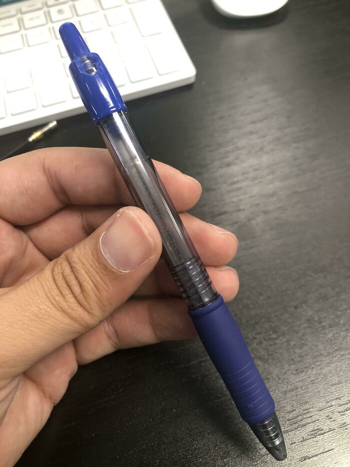 Mano sosteniendo un bolígrafo sin tinta sobre un escritorio con teclado al fondo, día peor en el trabajo.