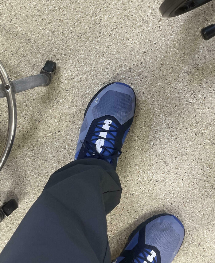 Persona con un día peor en el trabajo usando zapatos deportivos azules en un suelo de oficina gris claro.