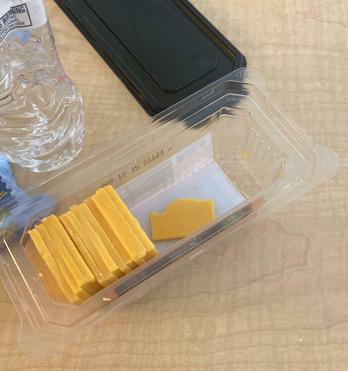 Queso en rebanadas parcialmente comido en empaque plástico junto a botella de agua en escritorio de oficina.