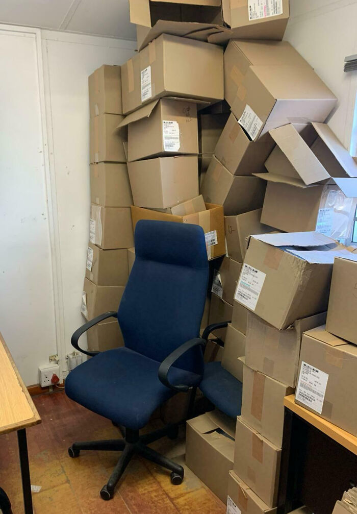 Silla de oficina rodeada por muchas cajas apiladas en espacio reducido, mostrando personas con un día peor en el trabajo.