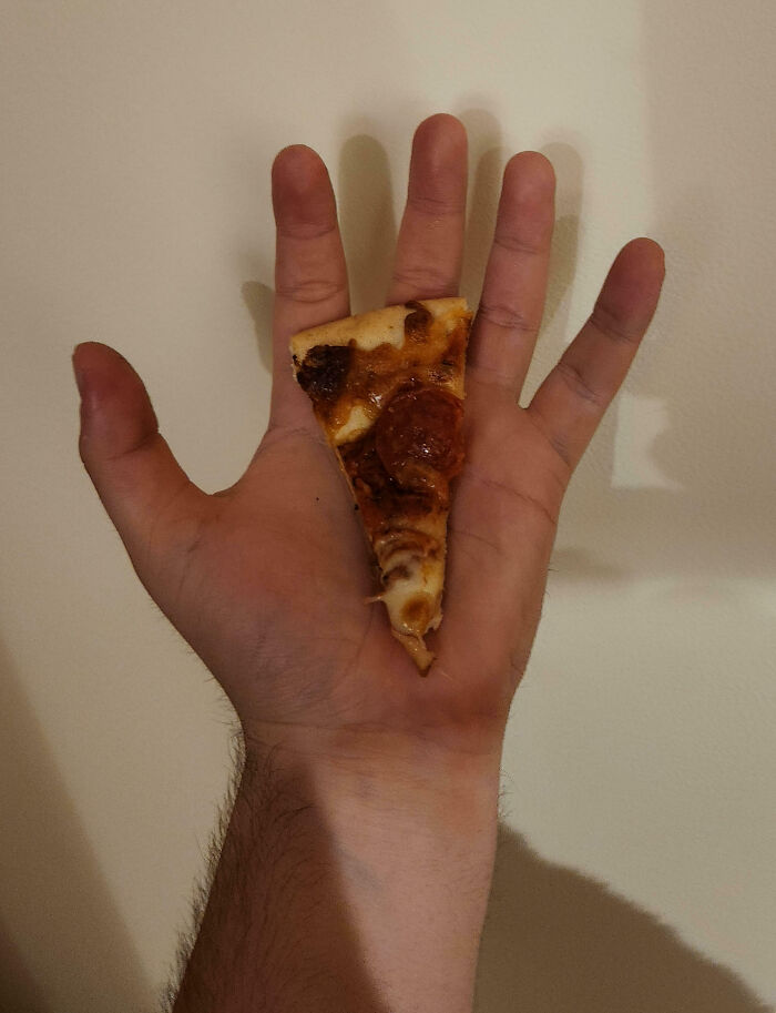 Mano sosteniendo una pequeña porción de pizza, una imagen que refleja un día peor en el trabajo para algunas personas.