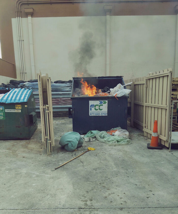 Contenedor de basura en llamas en área de trabajo, mostrando un día peor en el trabajo con fuego y desorden visible.