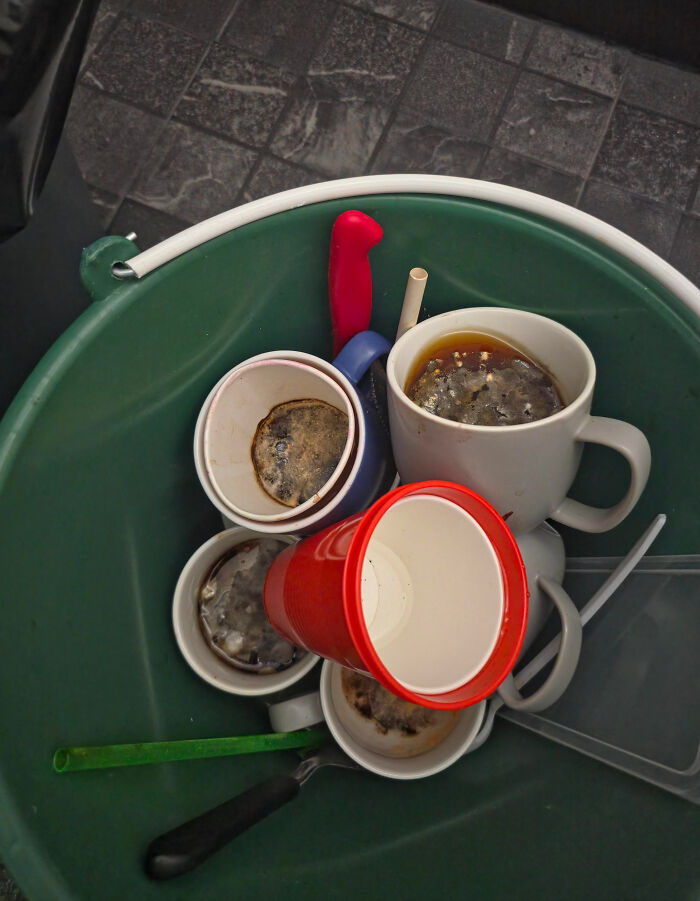 Tazas sucias con café viejo en un bote de basura, mostrando un día peor en el trabajo.