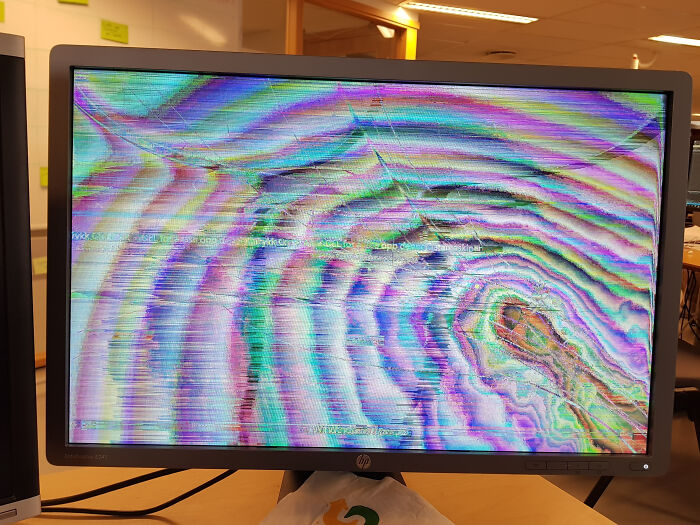 Pantalla de ordenador con fallo gráfico colorido mostrando un día peor en el trabajo para personas en oficina moderna.