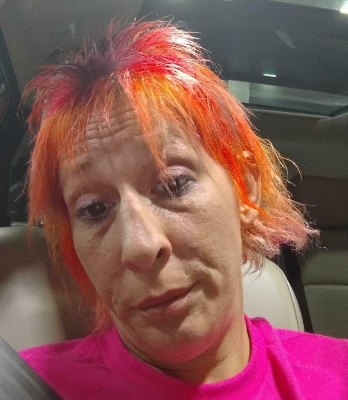 Mujer con expresión de arrepentimiento y cabello teñido en colores rojo y naranja después de salir del salón de belleza.
