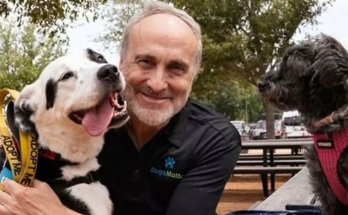 Hombre sonriente abrazando a perro feliz en parque, mostrando publicaciones reconfortantes para distraerte del mundo actual.