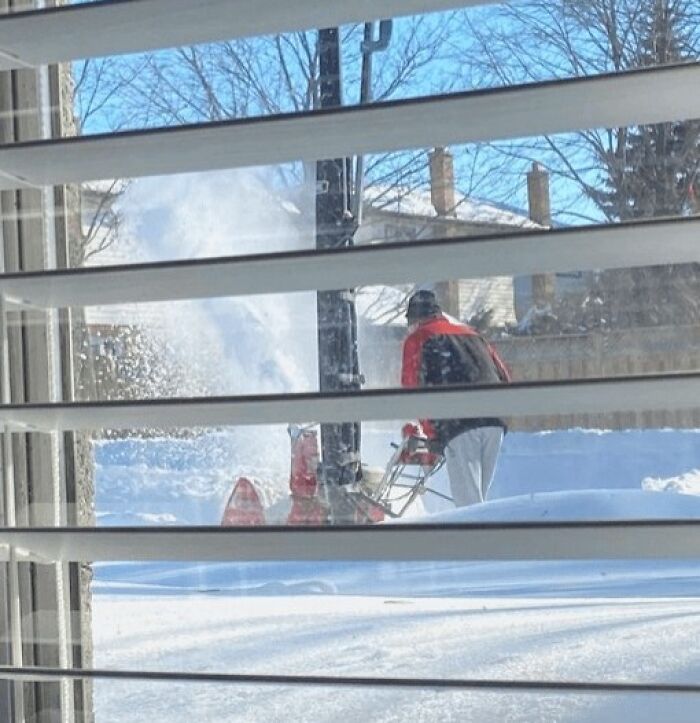 Persona quitando nieve afuera mientras se ve desde una ventana, imagen reconfortante para distraerte del mundo actual.