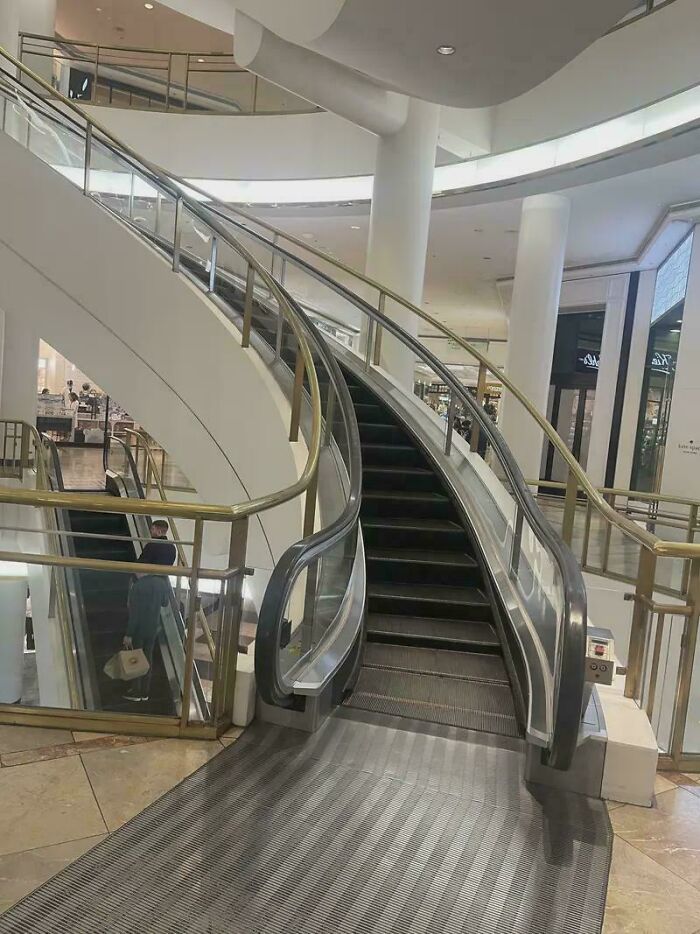 Escalera mecánica vacía en centro comercial moderno con barandales de metal y diseño arquitectónico llamativo, datos fascinantes.