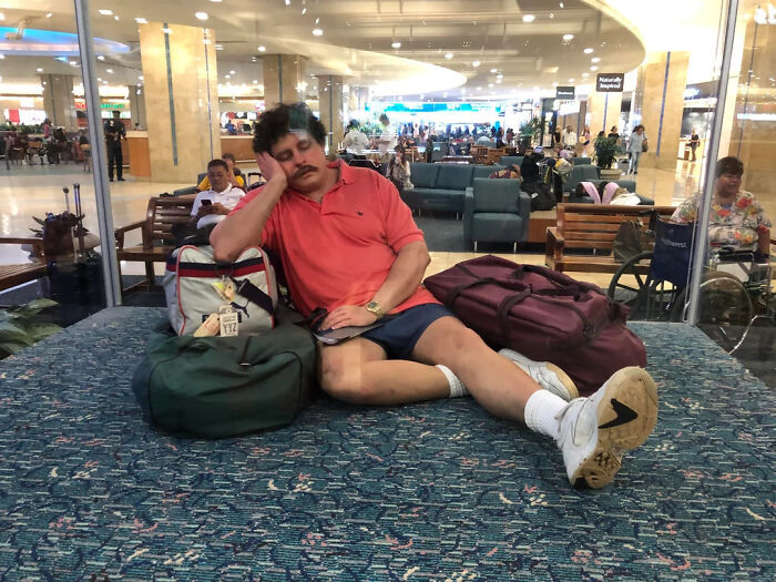 Hombre descansando en aeropuerto rodeado de equipaje, mostrando datos fascinantes de viajes y esperas largas.