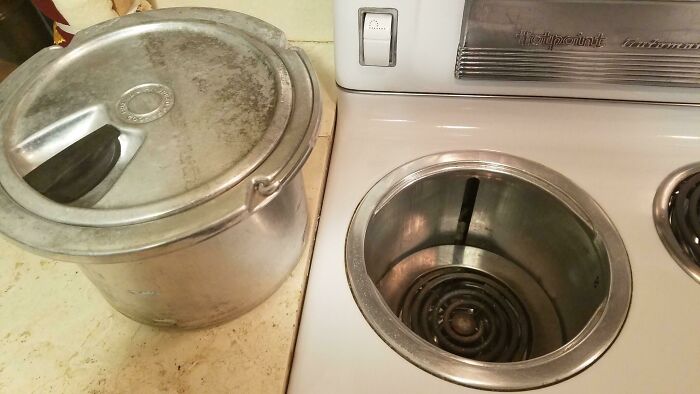 Olla de metal vintage junto a una cocina antigua eléctrica, mostrando objetos cotidianos de la década de 1950.
