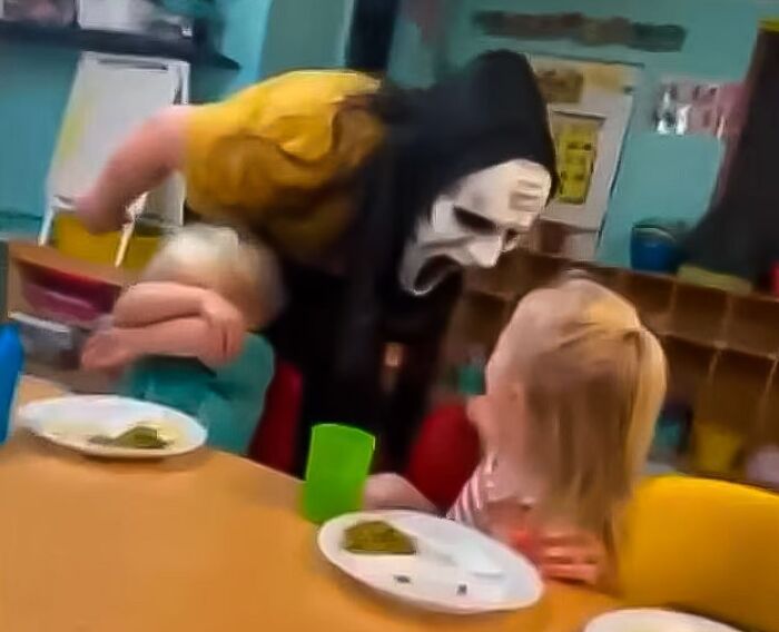 Persona con disfraz aterrador cerca de niños en comedor, mostrando comportamiento inapropiado en el trabajo y riesgo de despido.