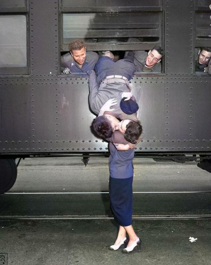 Pareja besándose apasionadamente en un tren mientras amigos observan, mostrando vida cotidiana en la década de 1950.
