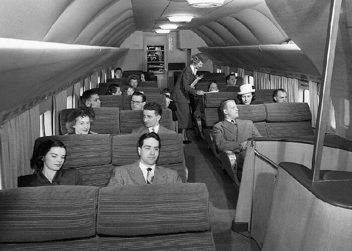 Pasajeros vestidos elegantemente en un avión de la década de 1950, mostrando la vida cotidiana en ese tiempo.
