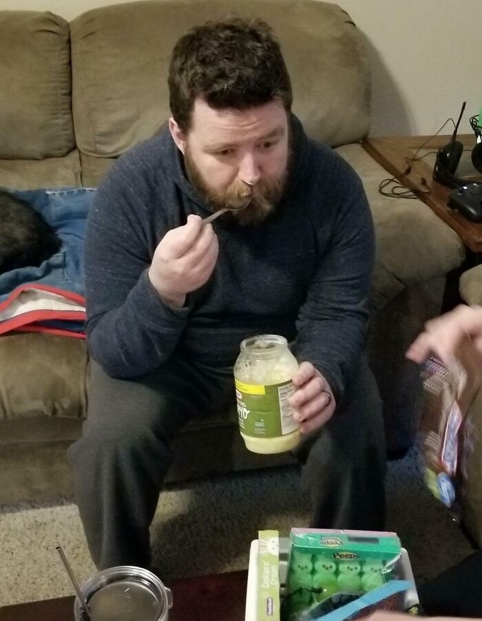 Hombre divertido comiendo mayonesa directamente del frasco en sala, mostrando momentos graciosos de padres divertidos. Hombre divertido comiendo mayonesa directamente del frasco en sala, mostrando momentos graciosos de padres divertidos.