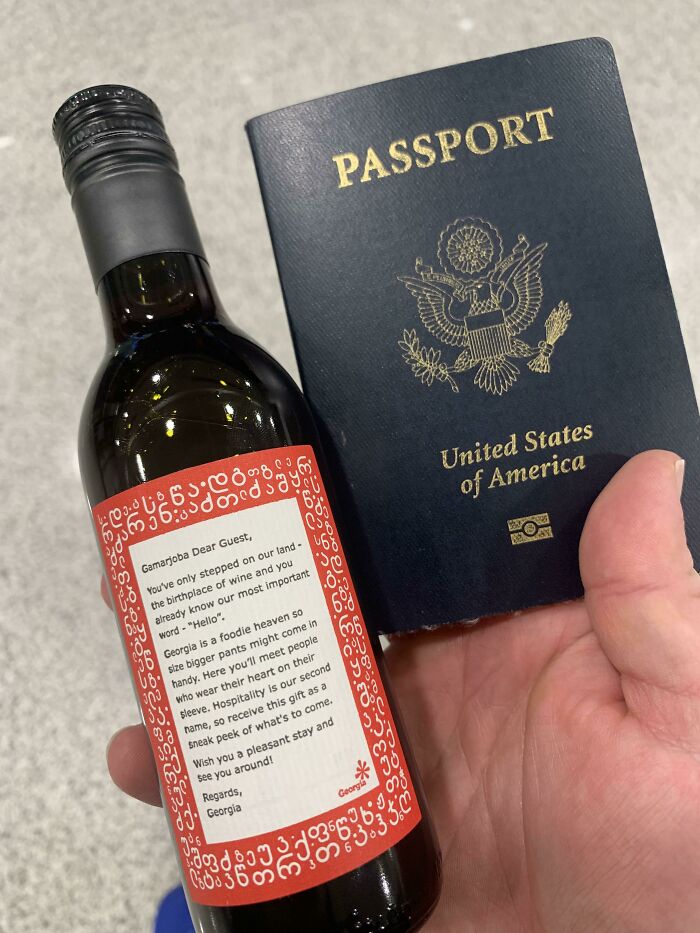 Botella de vino con mensaje de bienvenida y pasaporte de Estados Unidos en mano, mostrando detalles ingeniosos en la vida cotidiana.