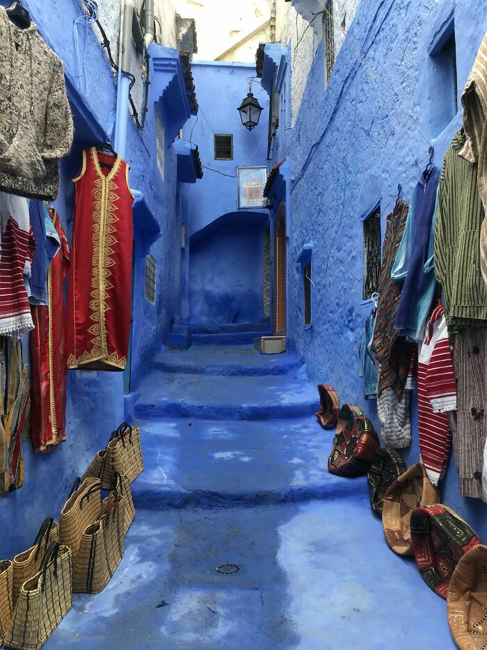 Calle estrecha pintada de azul con ropa y artesanías tradicionales, mostrando detalles ingeniosos en la vida cotidiana.