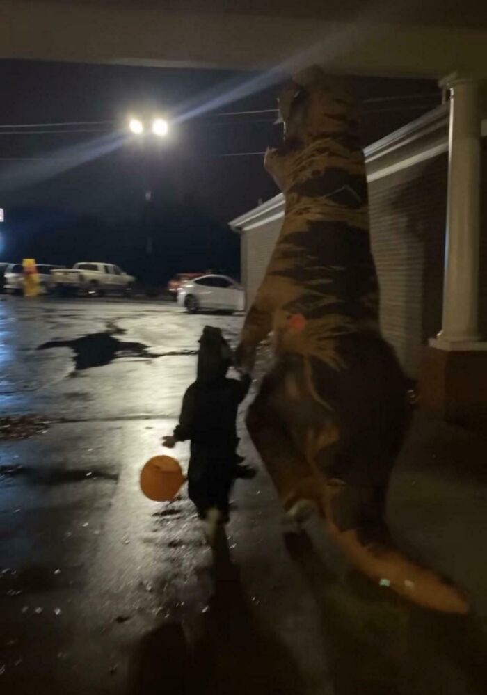 Padre disfrazado de dinosaurio divirtiéndose con su hijo en momento divertido y cariñoso de crianza nocturna.