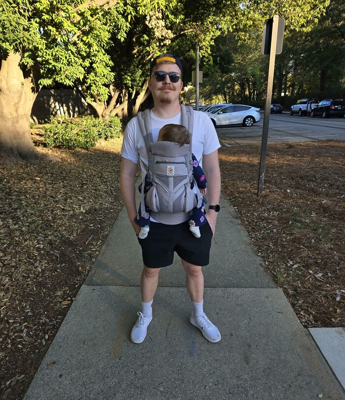 Padre en parque llevando a su bebé en portabebé, mostrando momentos divertidos y tiernos de paternidad activa.