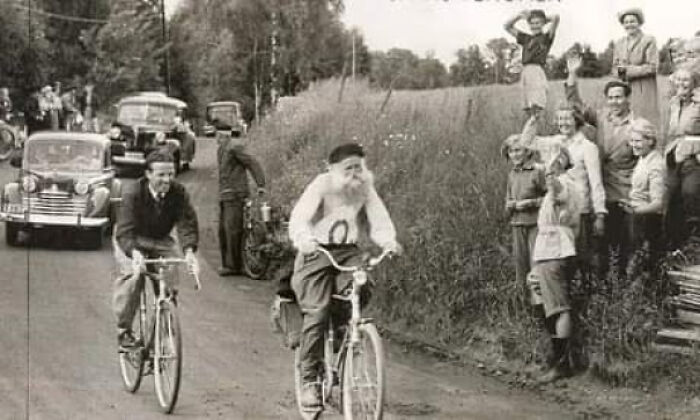 Celebración y curiosidades en una carrera de bicicletas vintage con espectadores sorprendidos y automóviles antiguos de fondo.