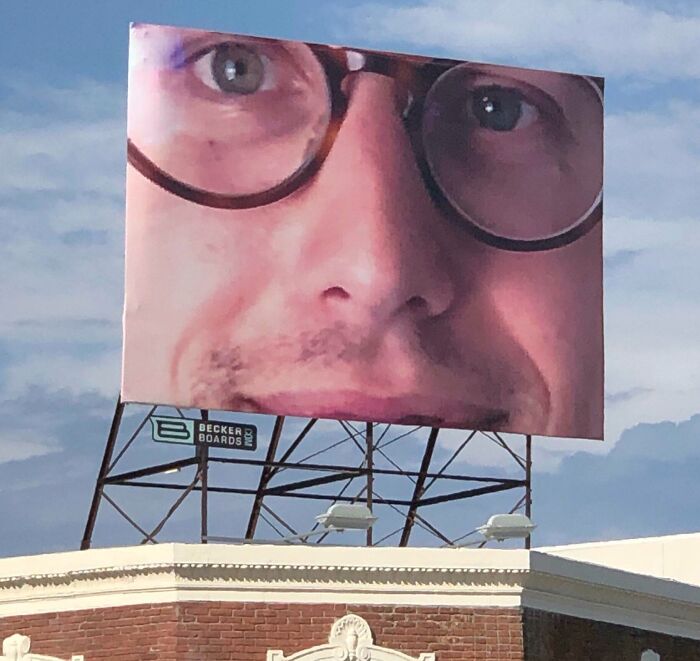 Gran cartel publicitario con imagen ampliada de un rostro con gafas, ejemplo de divertidos fallos publicitarios.