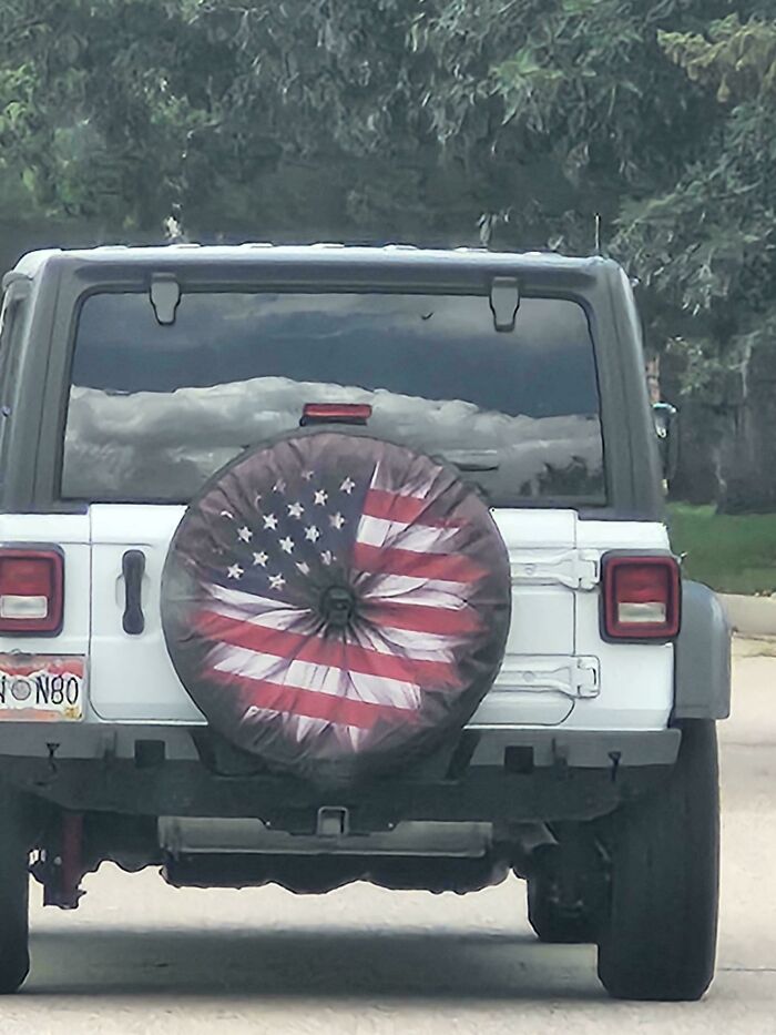 Jeep blanco estacionado con funda de llanta trasera rota con la bandera de EE. UU., ejemplo de intento fallido y planes del universo.