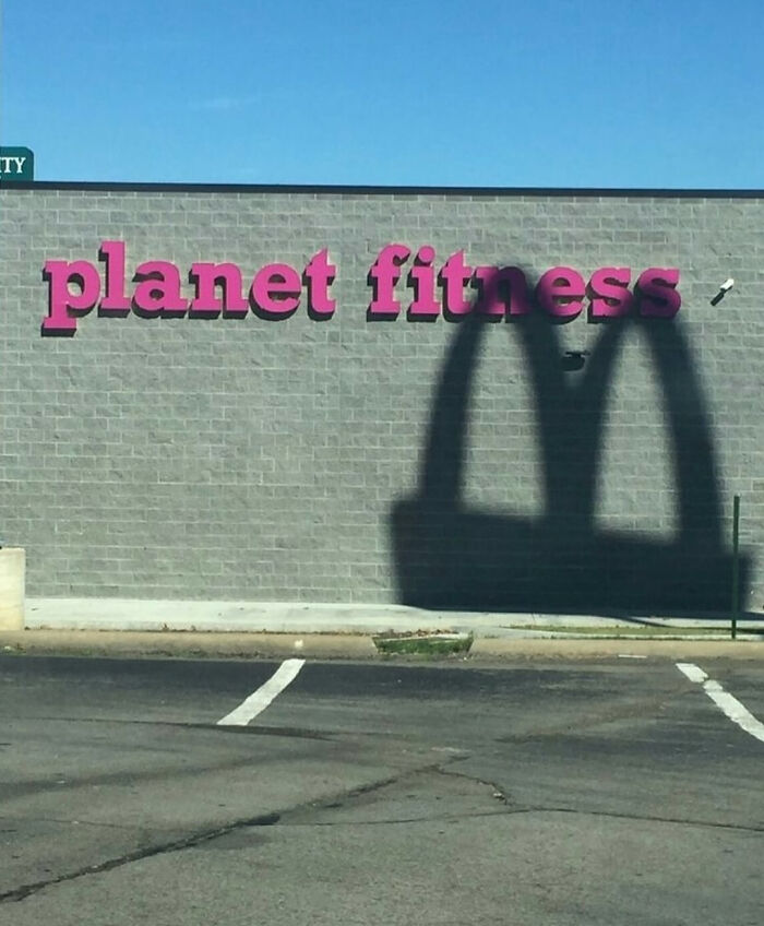 Sombra del logo de McDonald's proyectada sobre el letrero de Planet Fitness en un intento fallido del universo.