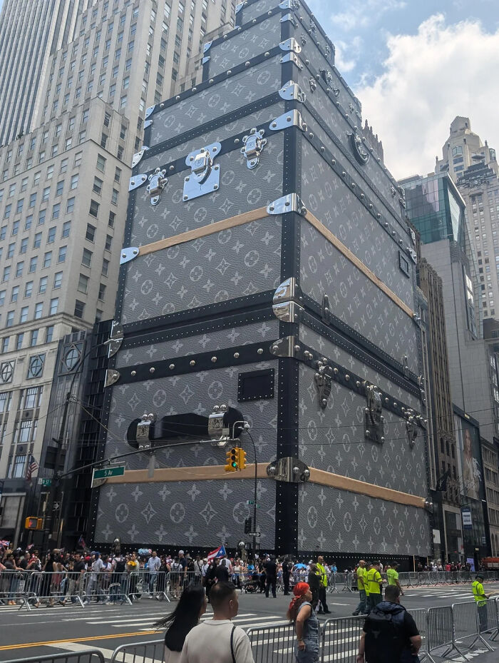 Edificio gigante con diseño de maleta de lujo en ciudad con multitud y barricadas en la calle, cosas interesantes compartidas.