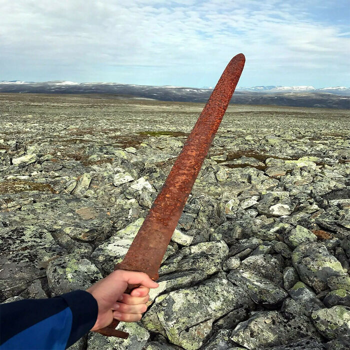 Espada oxidada antigua en mano sobre un terreno rocoso con montañas al fondo, datos históricos interesantes.