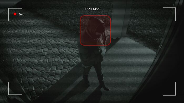 Persona con sudadera con capucha grabada por cámara de seguridad mientras camina de noche, casos detectives privados.