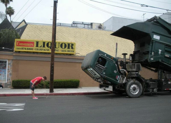 Hombre mirando con curiosidad un camión volquete inclinado en la calle, imagen realmente incómoda pero divertida.
