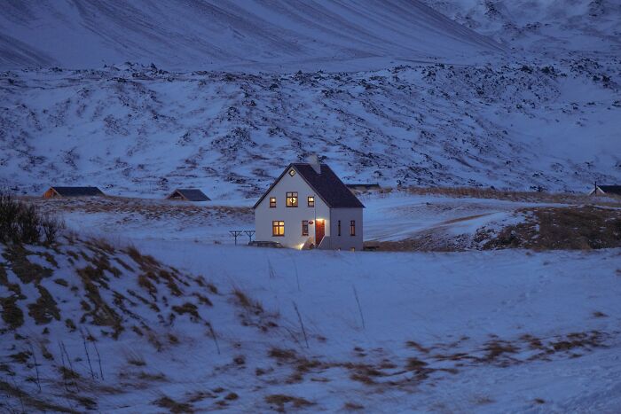 Casa iluminada en paisaje nevado al atardecer, evocando historias desquiciadas y deprimentes sobre familias.