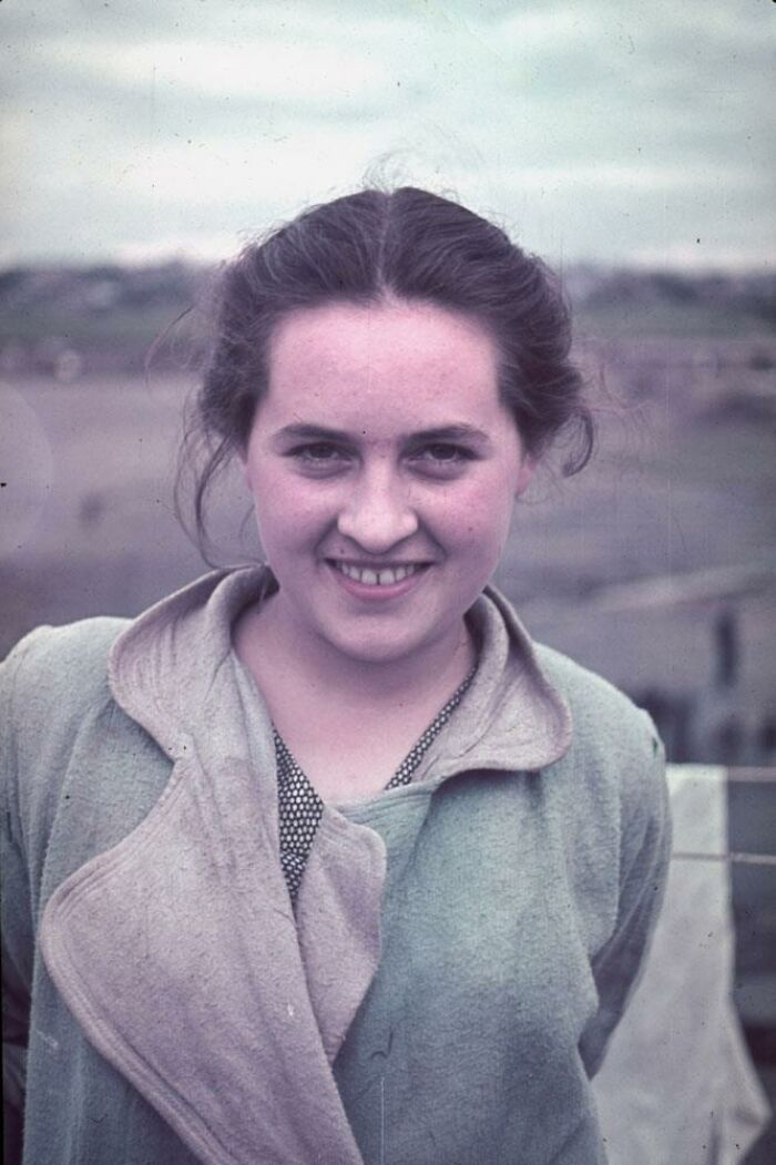 Mujer joven sonriente con abrigo verde en paisaje rural, una foto inquietante que parece normal a simple vista.