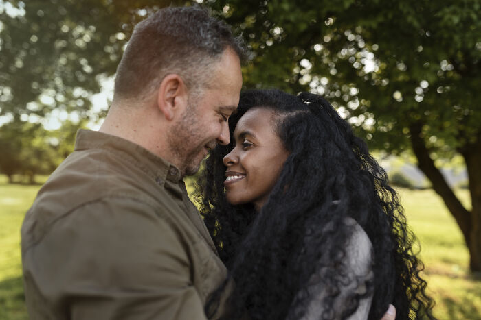 Pareja sonriente abrazándose en un parque al aire libre, mostrando afecto y conexión familiar sincera.