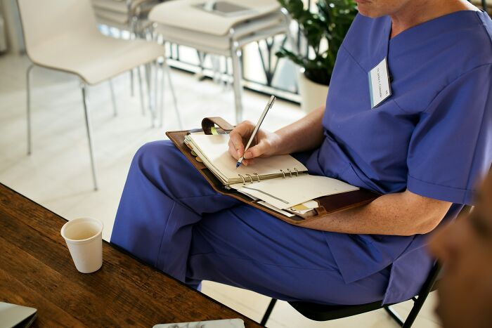 Persona con uniforme médico escribiendo en cuaderno en sala de espera, ilustrando cosas desquiciadas sobre sus familias.