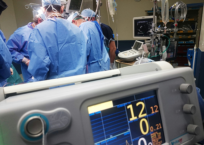 Equipo médico en quirófano realizando cirugía, con monitor mostrando signos vitales del paciente en primer plano.