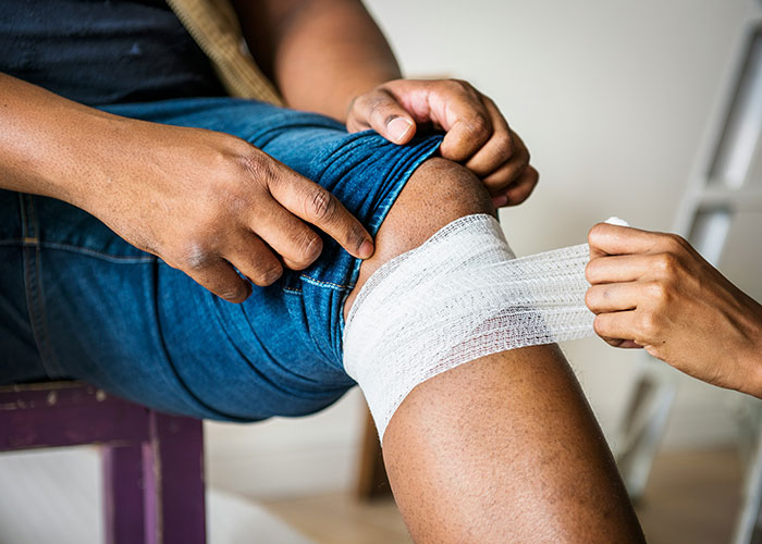 Persona con lesión en la rodilla siendo vendada por un médico en consulta, casos médicos que requieren atención temprana.